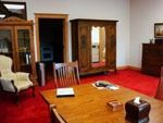 A wood-paneled room with a red carpet, a wooden table, chairs, an armchair, and large wooden storage cabinets.
