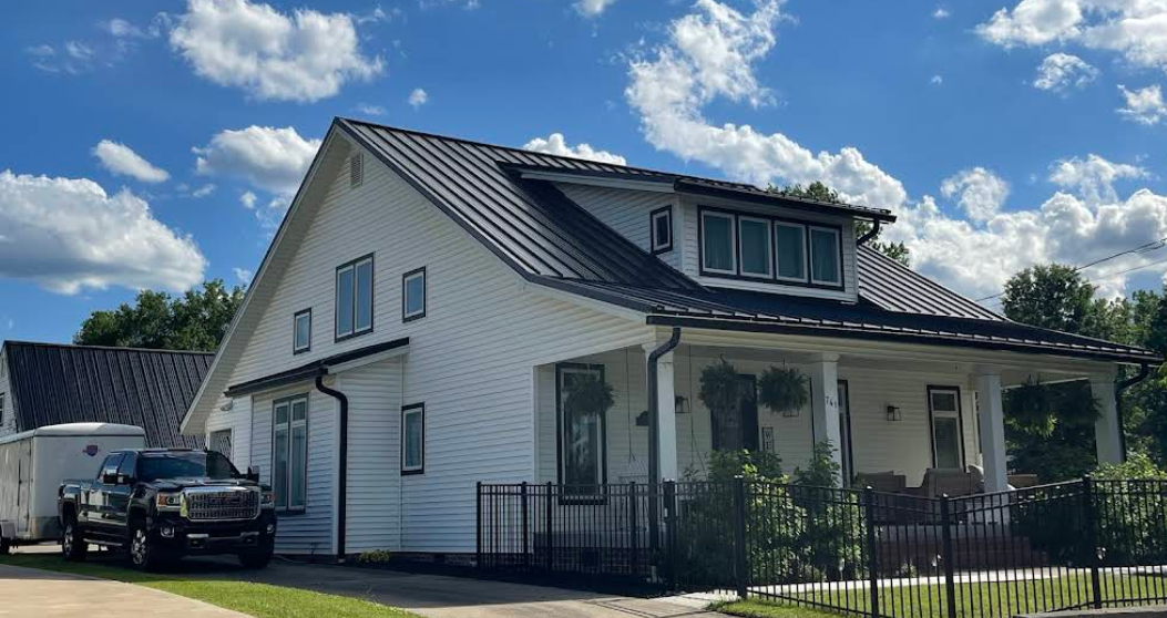 A white house with a black roof and a black truck parked in front of it.
