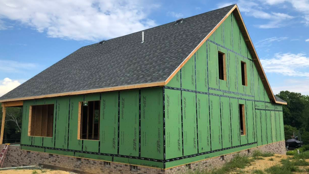 A house is being built with green siding and a gray roof.