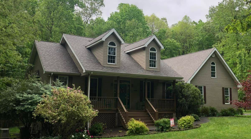 A large house with a large porch is surrounded by trees.