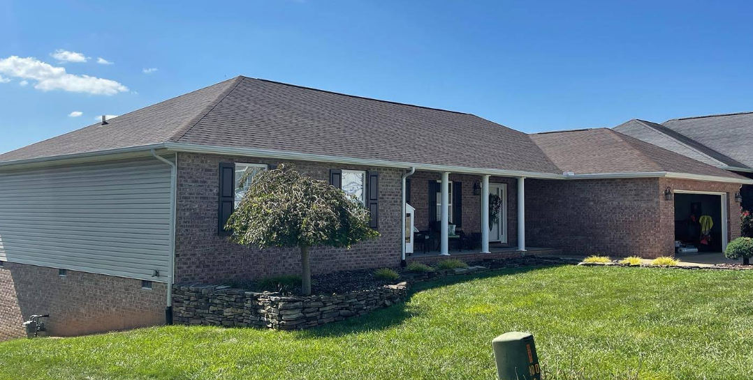 A brick house with a brown roof is sitting on top of a lush green lawn.