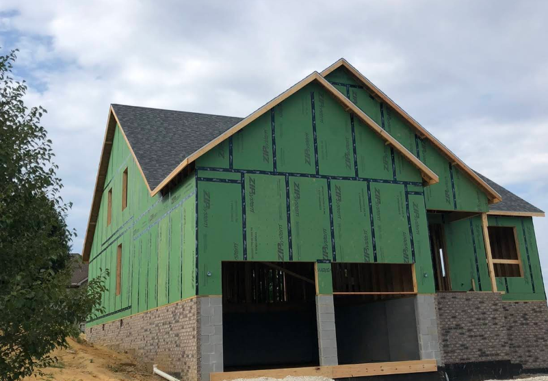 A house is being built with green siding and a roof.