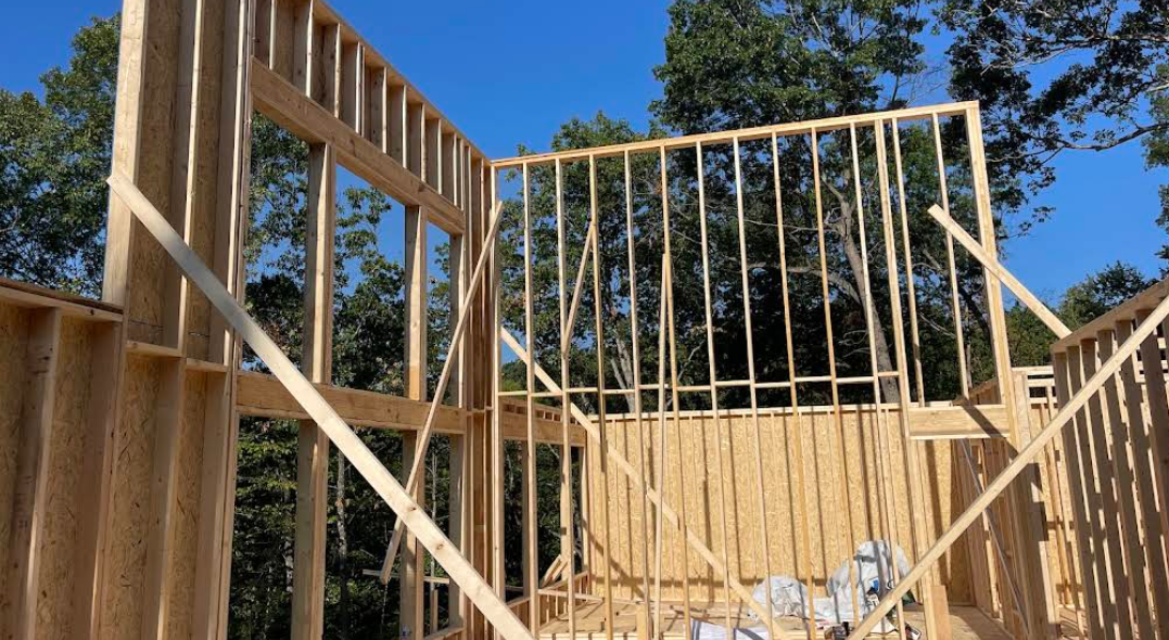 A house is being built with wooden beams and a blue sky in the background.