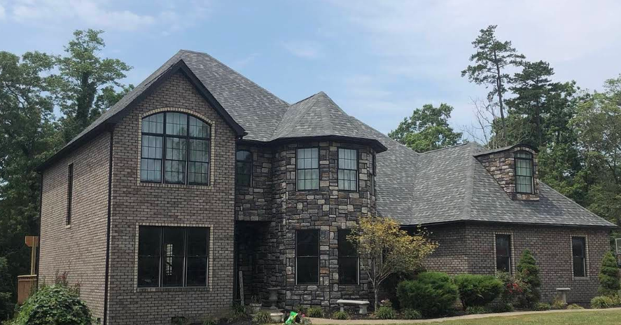 A large brick house with a gray roof is surrounded by trees.