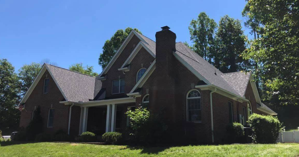 A large brick house with a chimney on the roof is sitting on top of a lush green lawn.