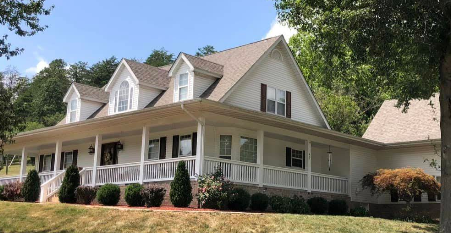 A large white house with a large porch is surrounded by trees.