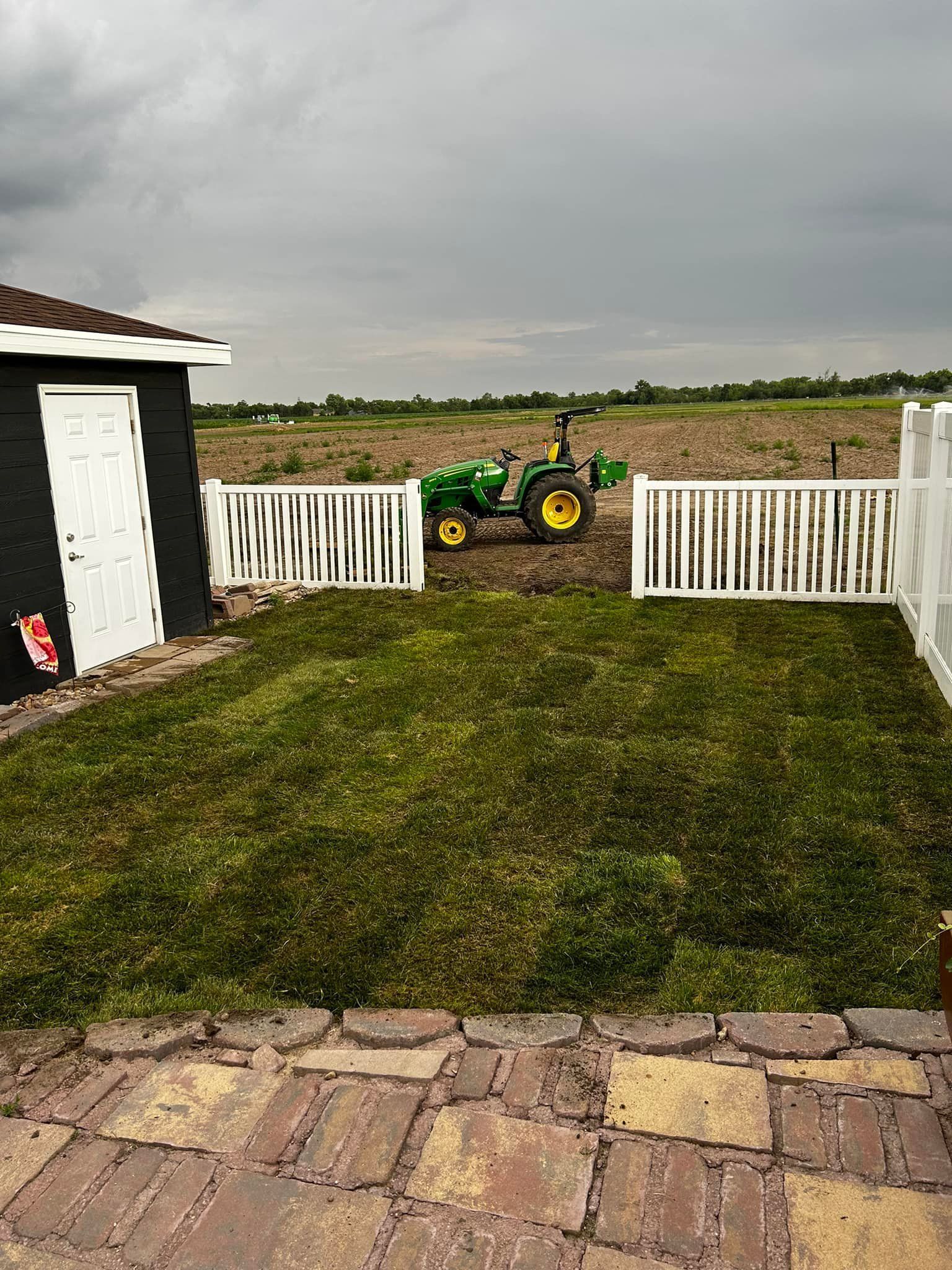 Small tractor in field behind white picket fence and grass, cloudy sky.