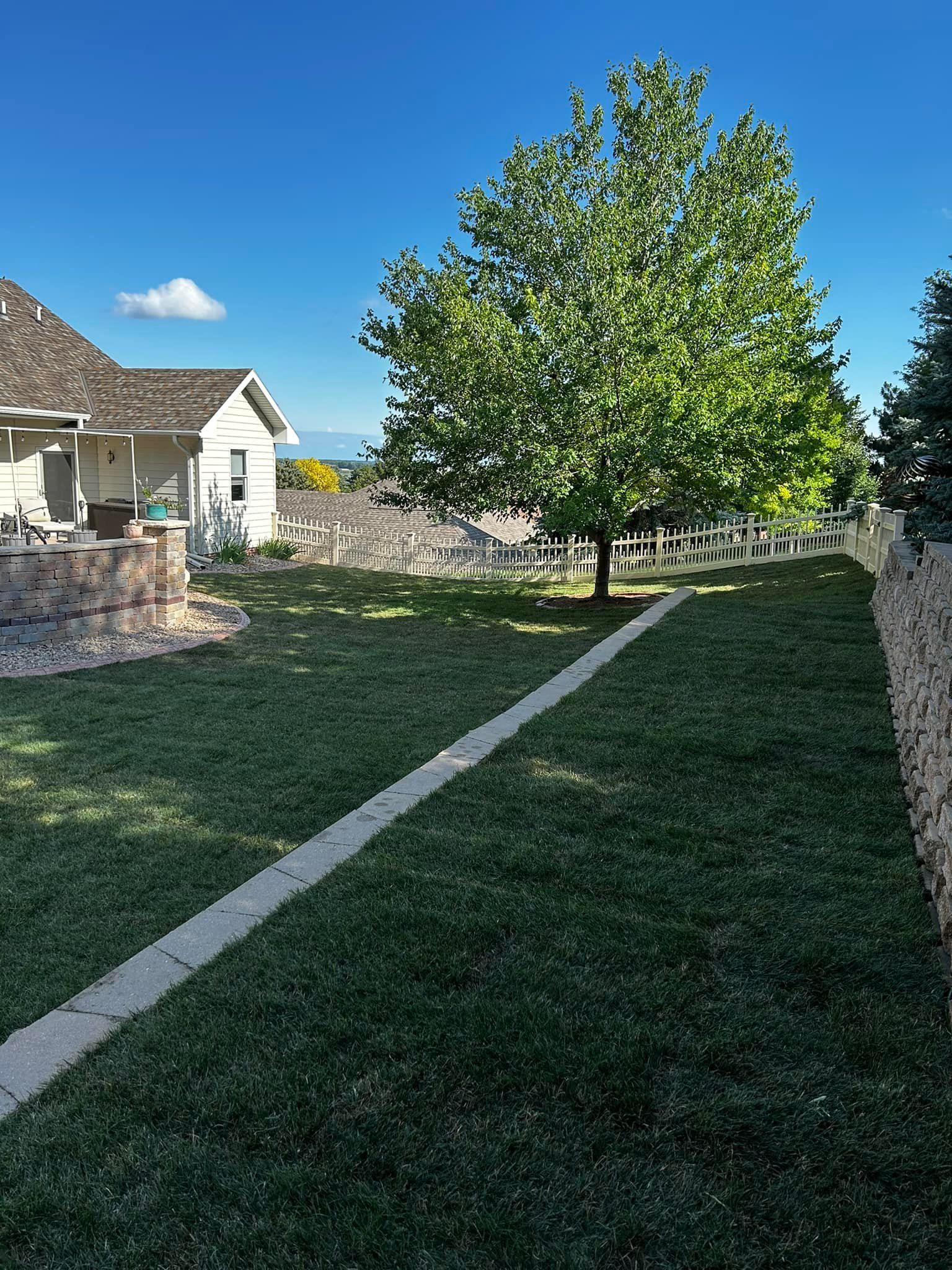 Lawn, white picket fence, tree, and small house under a bright blue sky.