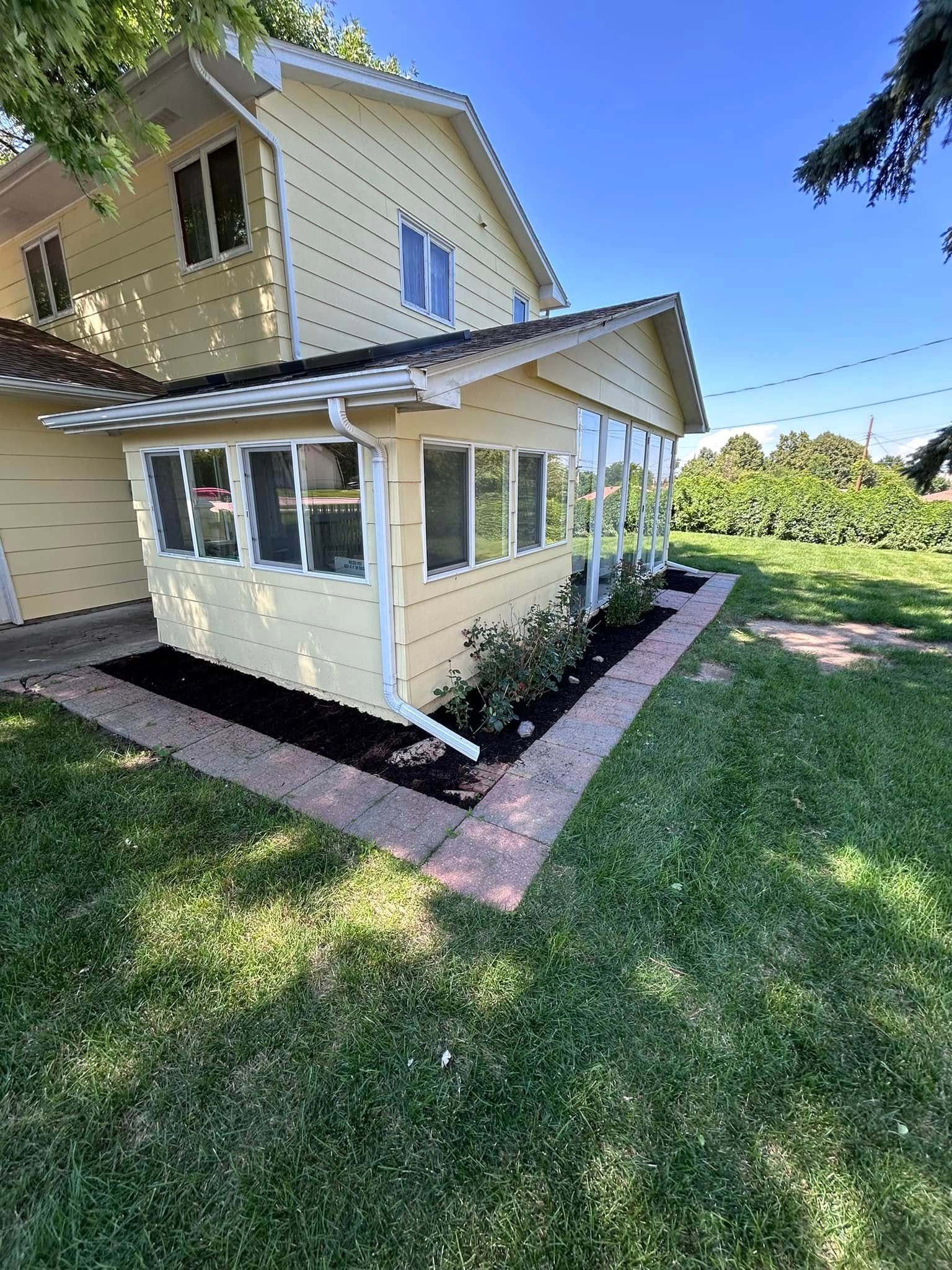 Yellow house with a sunroom and landscaping on a sunny day.