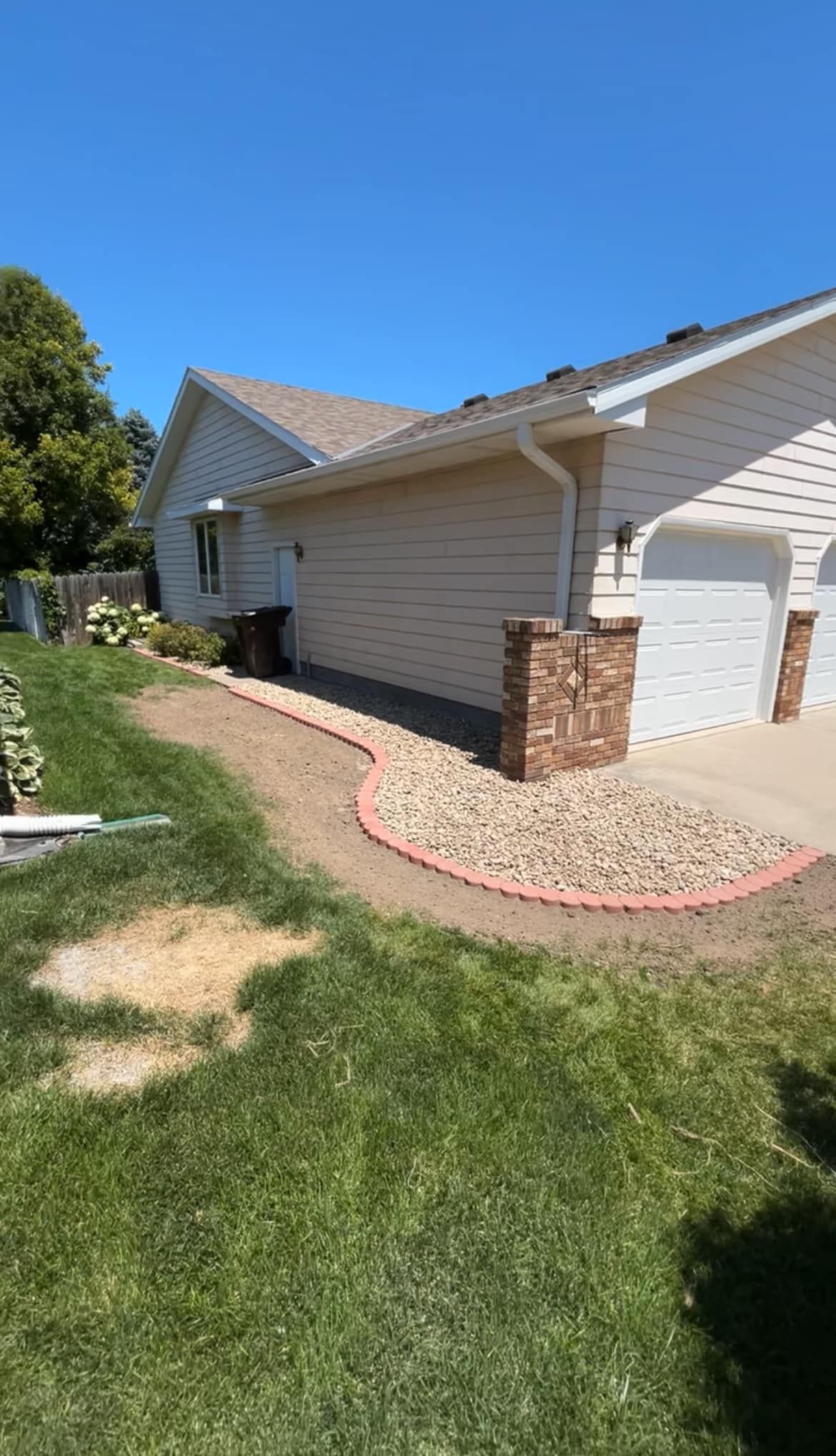 House exterior with gravel bed and brick border. Green grass, blue sky.