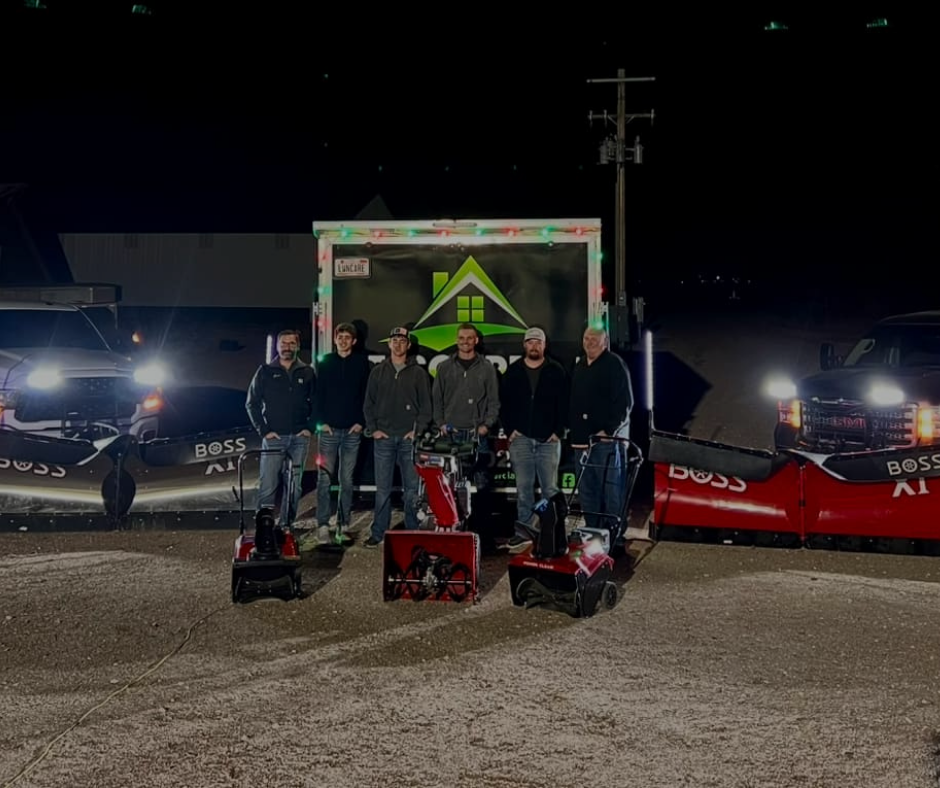 Group of men posing with snowblowers and trucks at night.