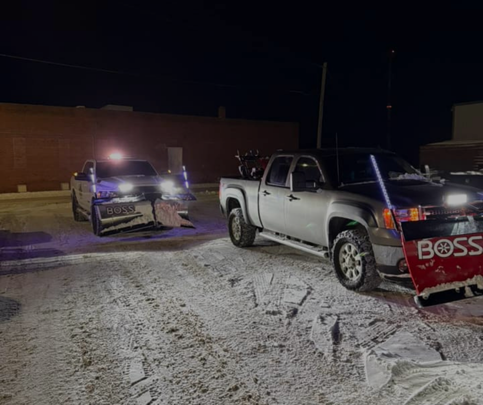 Two snowplow trucks clearing a snowy street at night.