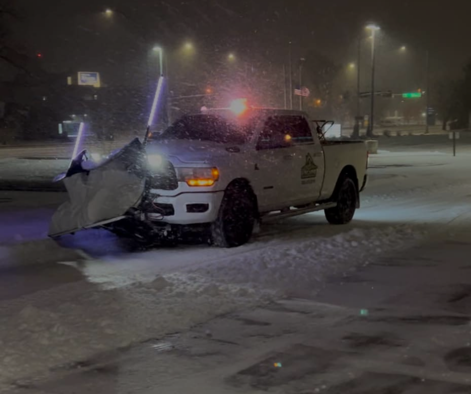 Snowplow clearing a snow-covered road at night. Truck with lights, plowing snow in a city.