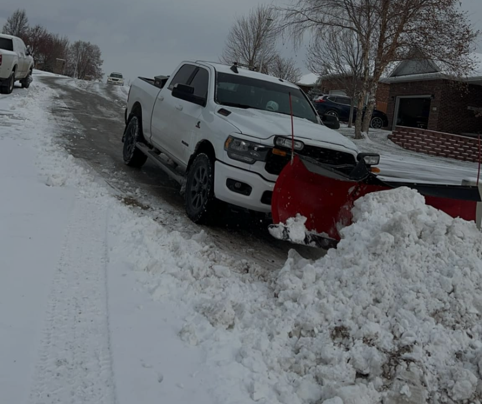 White pickup truck with snowplow clearing a snowy road.