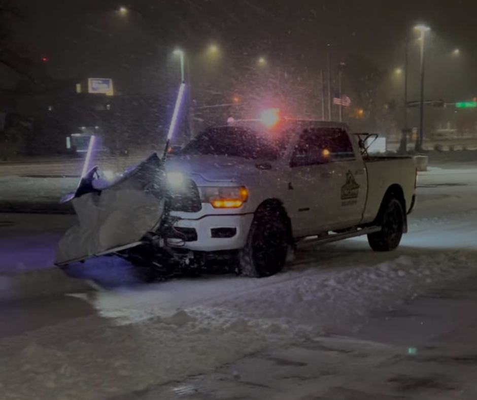 Snowplow clearing a snowy road at night with flashing lights and headlights.