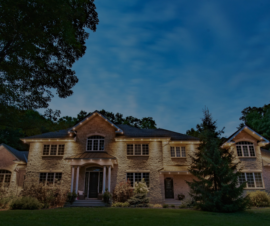 Large stone house illuminated at dusk, with a dark blue sky and trees surrounding it.