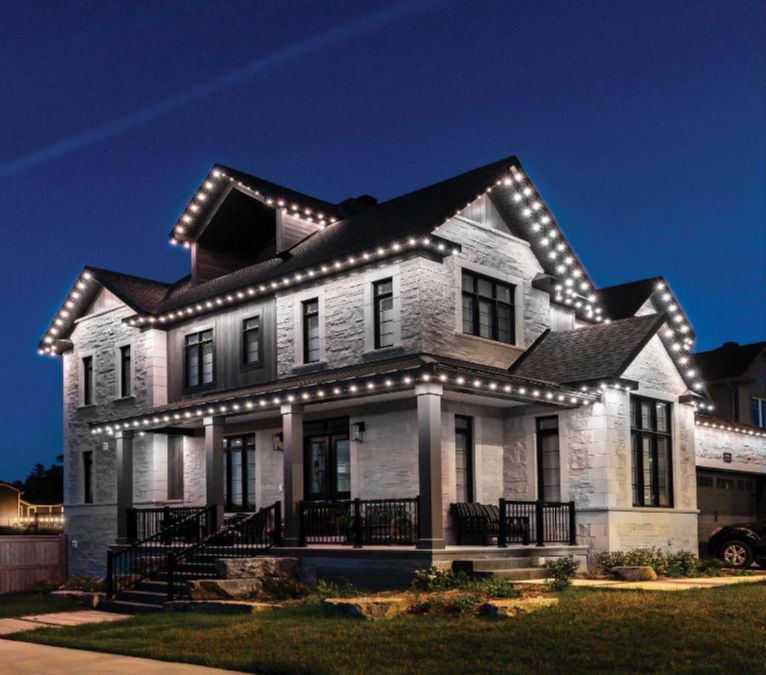 Two-story house with white lights outlining roof and porch against a dark blue sky.