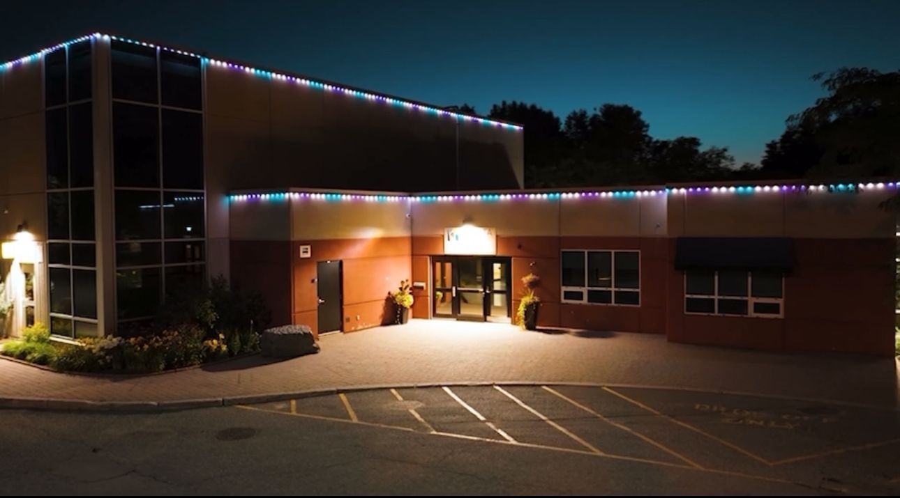 Building at dusk with colorful string lights outlining the roof. Front entrance is lit up.