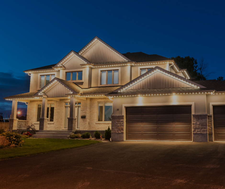 Two-story beige house with lit roofline at night, illuminated driveway and garage.