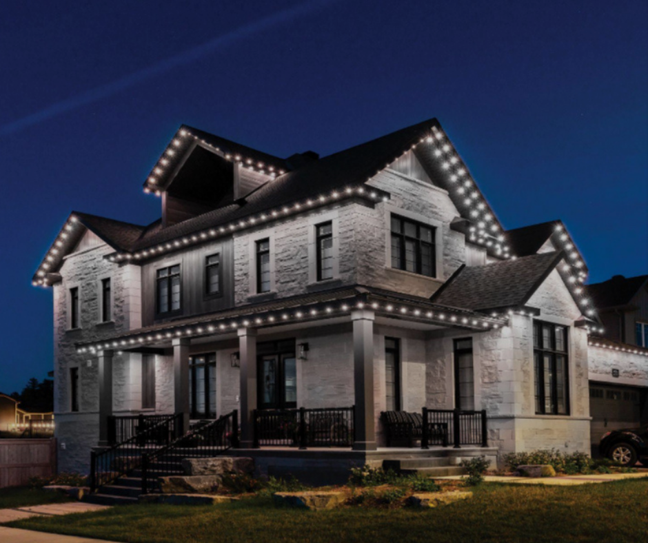 House with white brick exterior, lit with white string lights along the roofline and porch, at night.