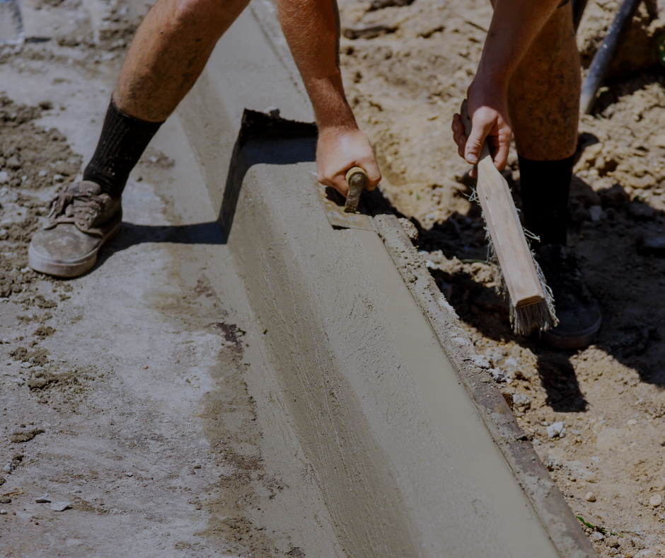Person smoothing wet concrete with a wooden tool to form a curb outdoors.