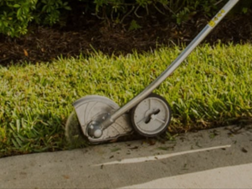 A string trimmer edging grass along a sidewalk.
