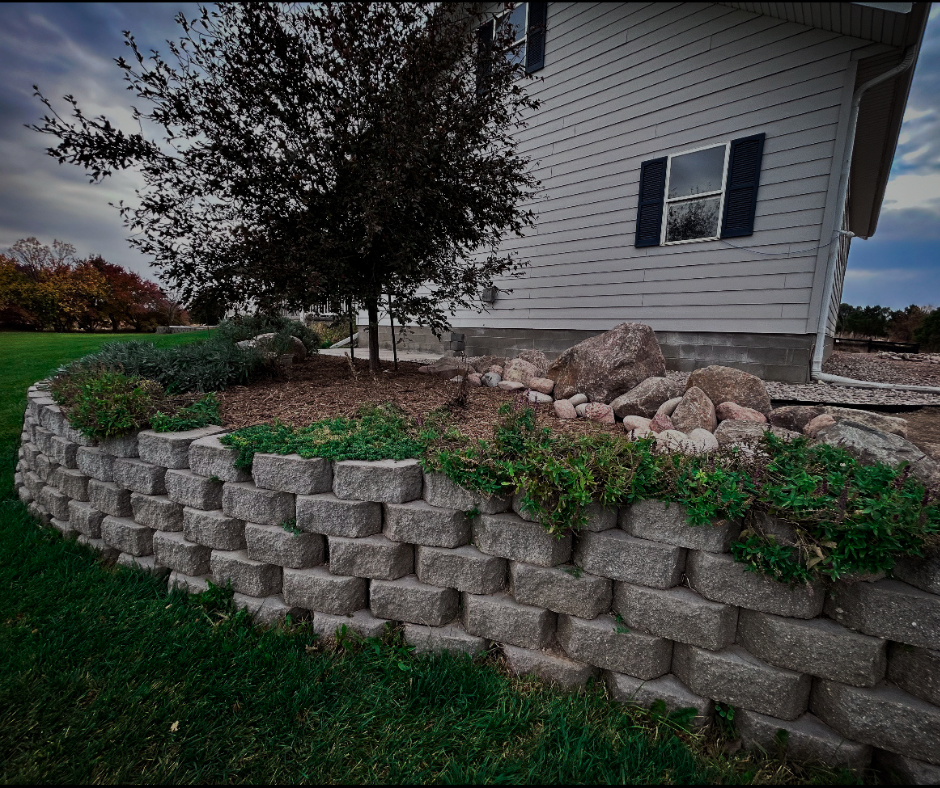 Stone retaining wall with greenery in front of a house.