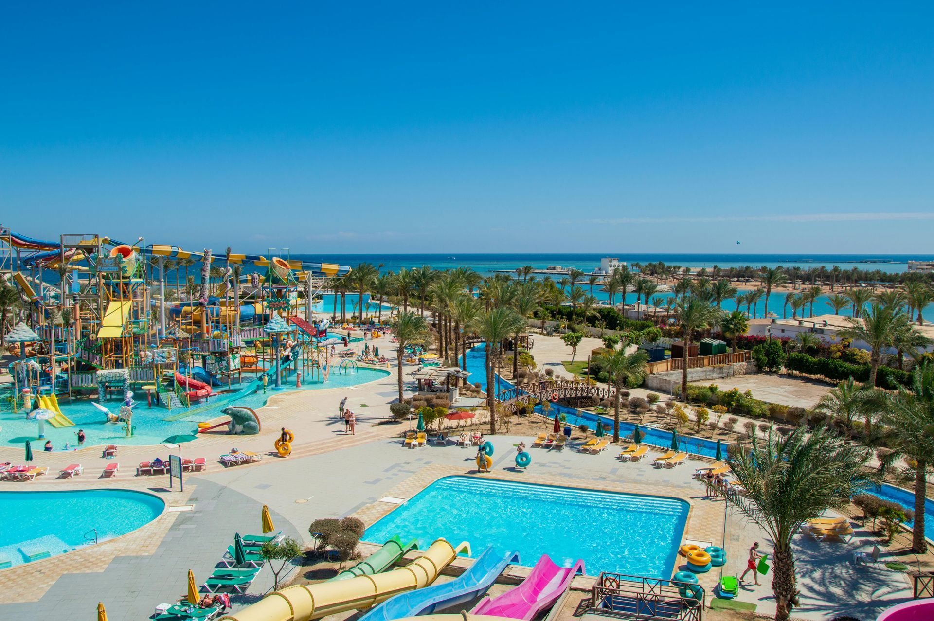 Bright, sunny view of a waterpark with many slides, pools, and people enjoying the day.