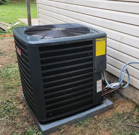 Gray air conditioning unit outside a white-sided building on a concrete pad, surrounded by grass.
