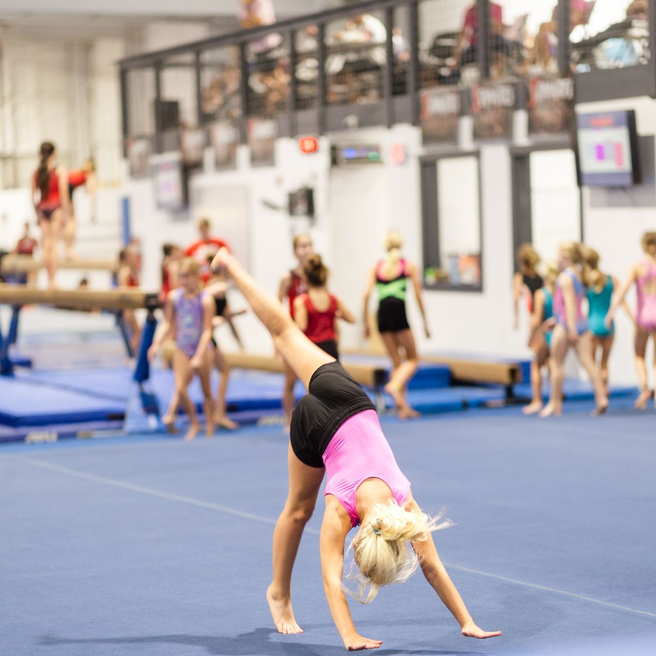 A young girl is doing a handstand on a balance beam in a gym.