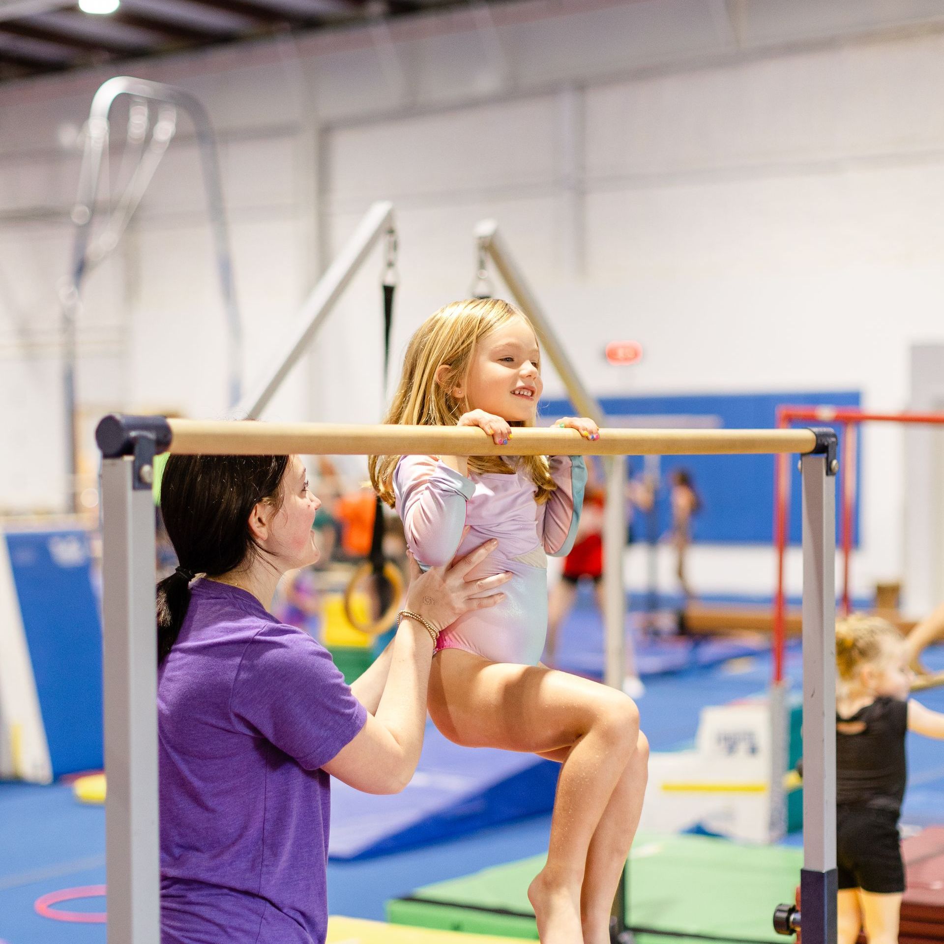 A little girl is sitting on a bar in a gym