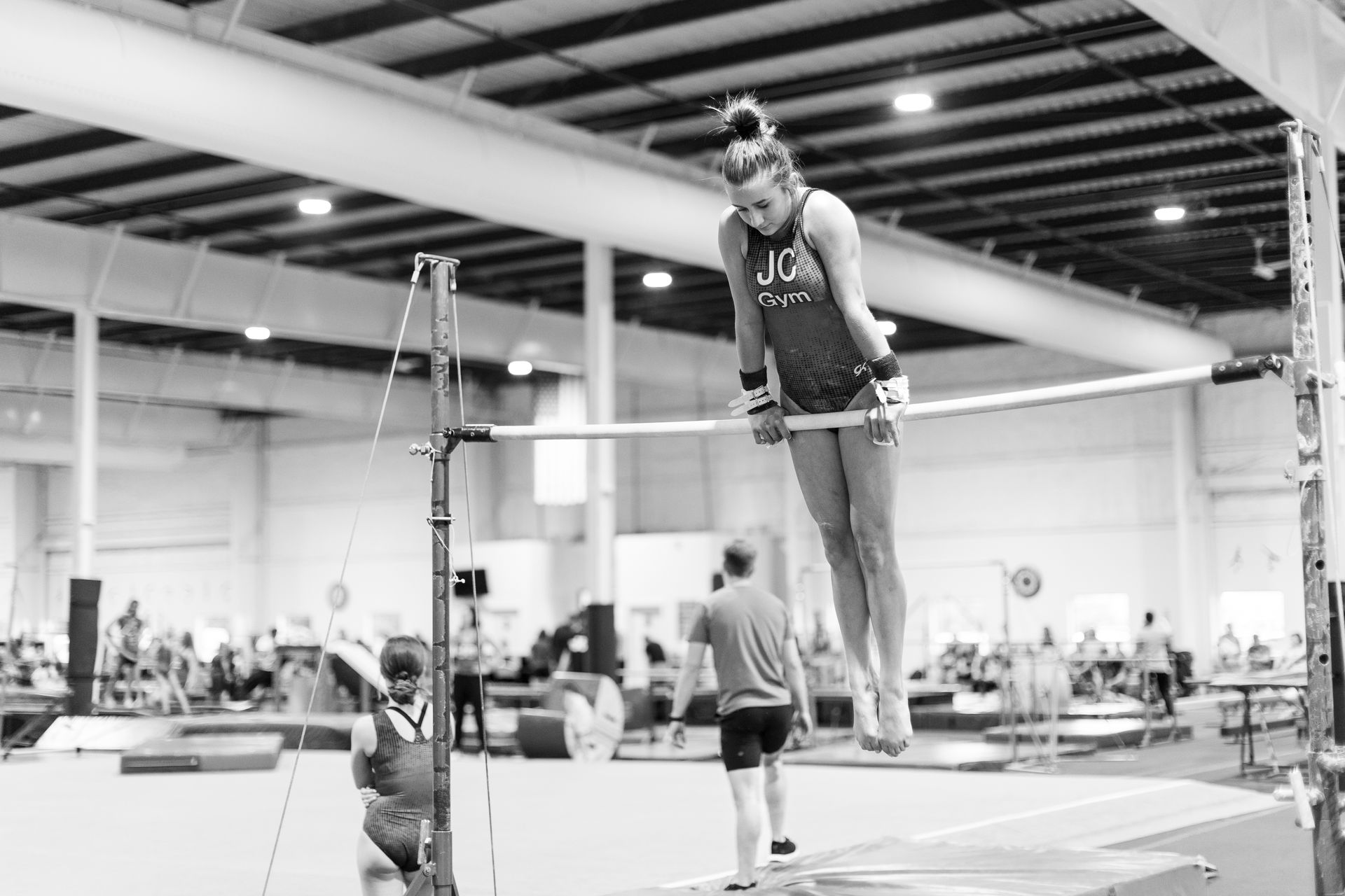 A female gymnast is doing a handstand on a parallel bars in a gym.