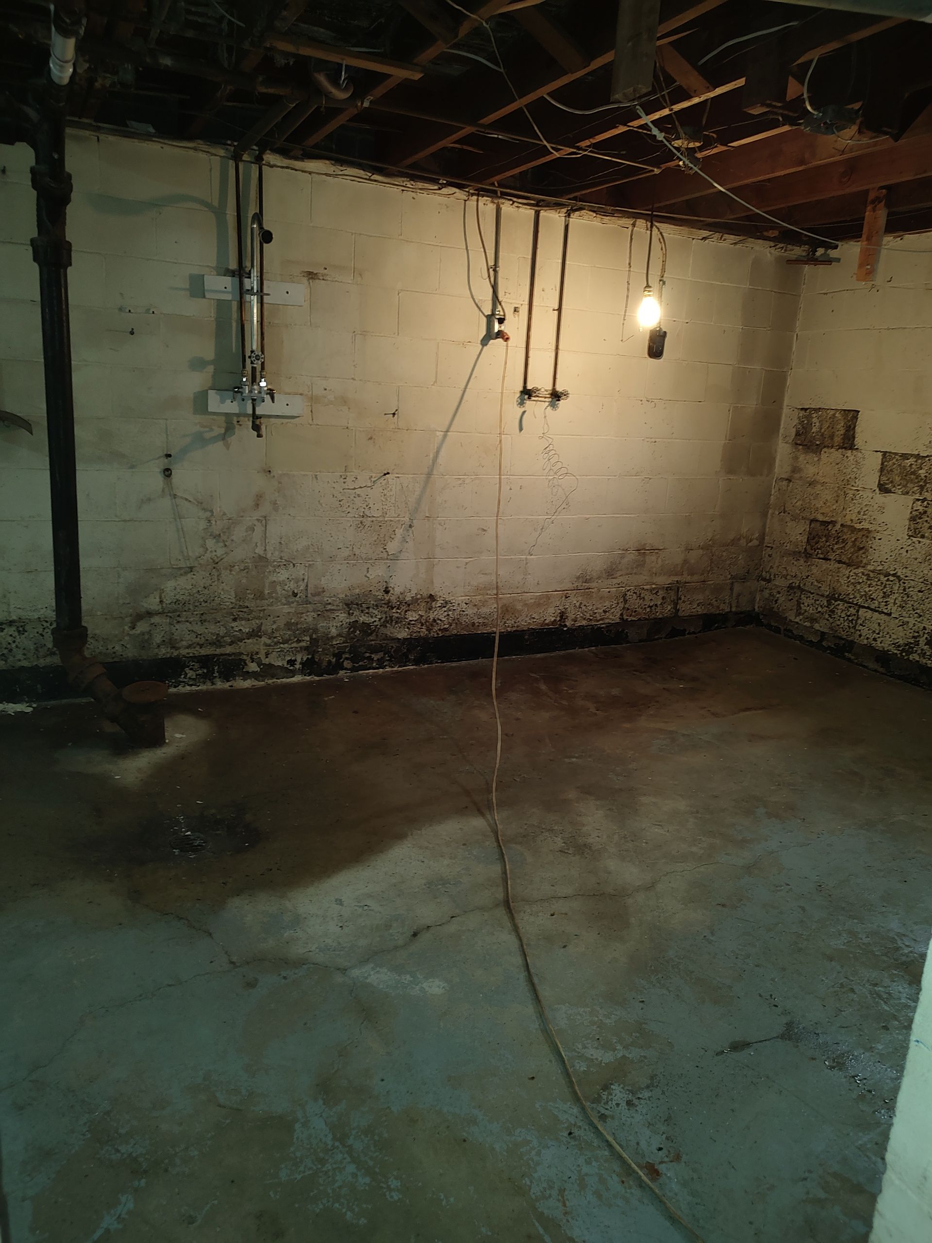 An empty basement with a light hanging from the ceiling.