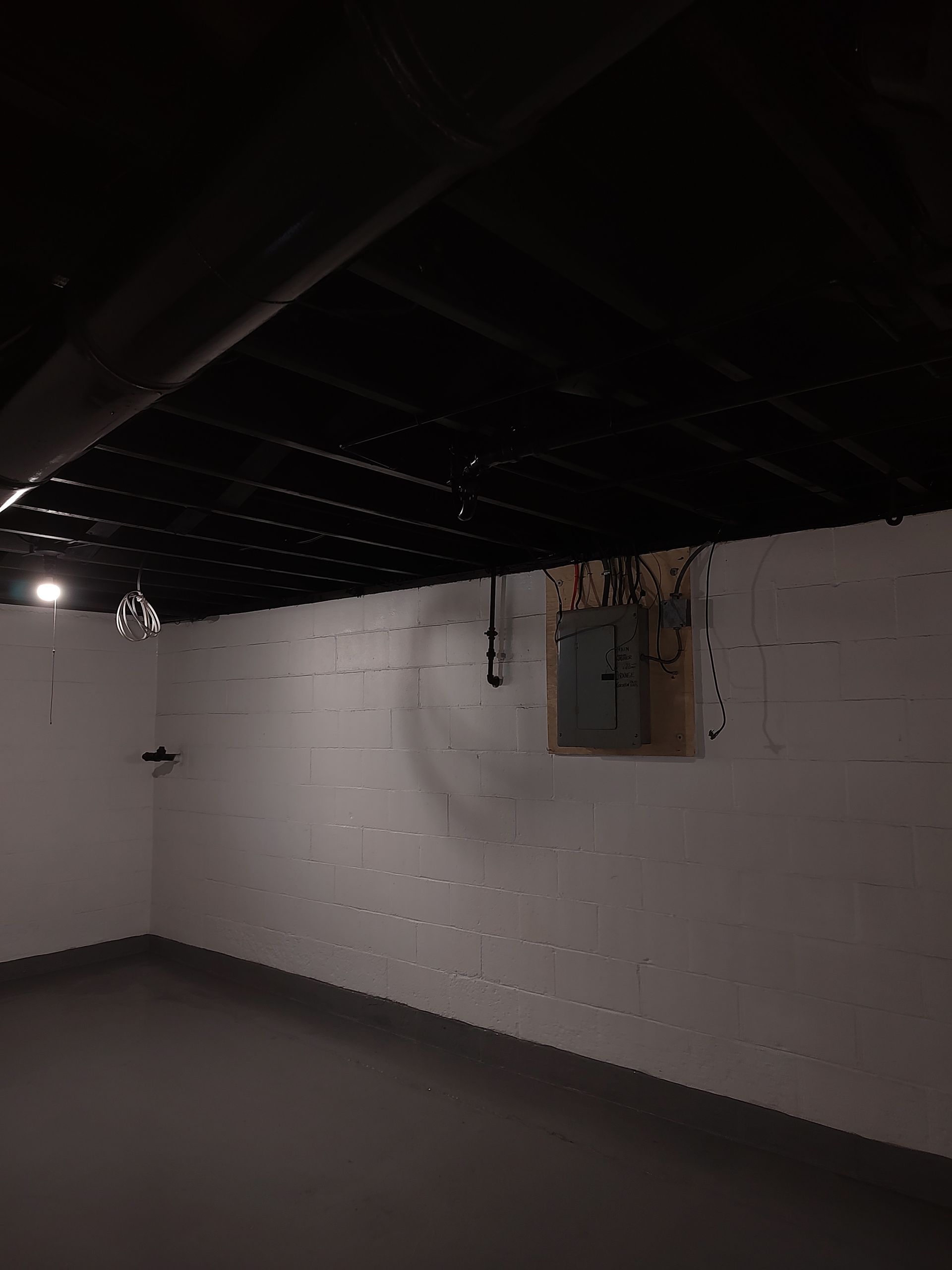 An empty basement with a black ceiling and white walls.