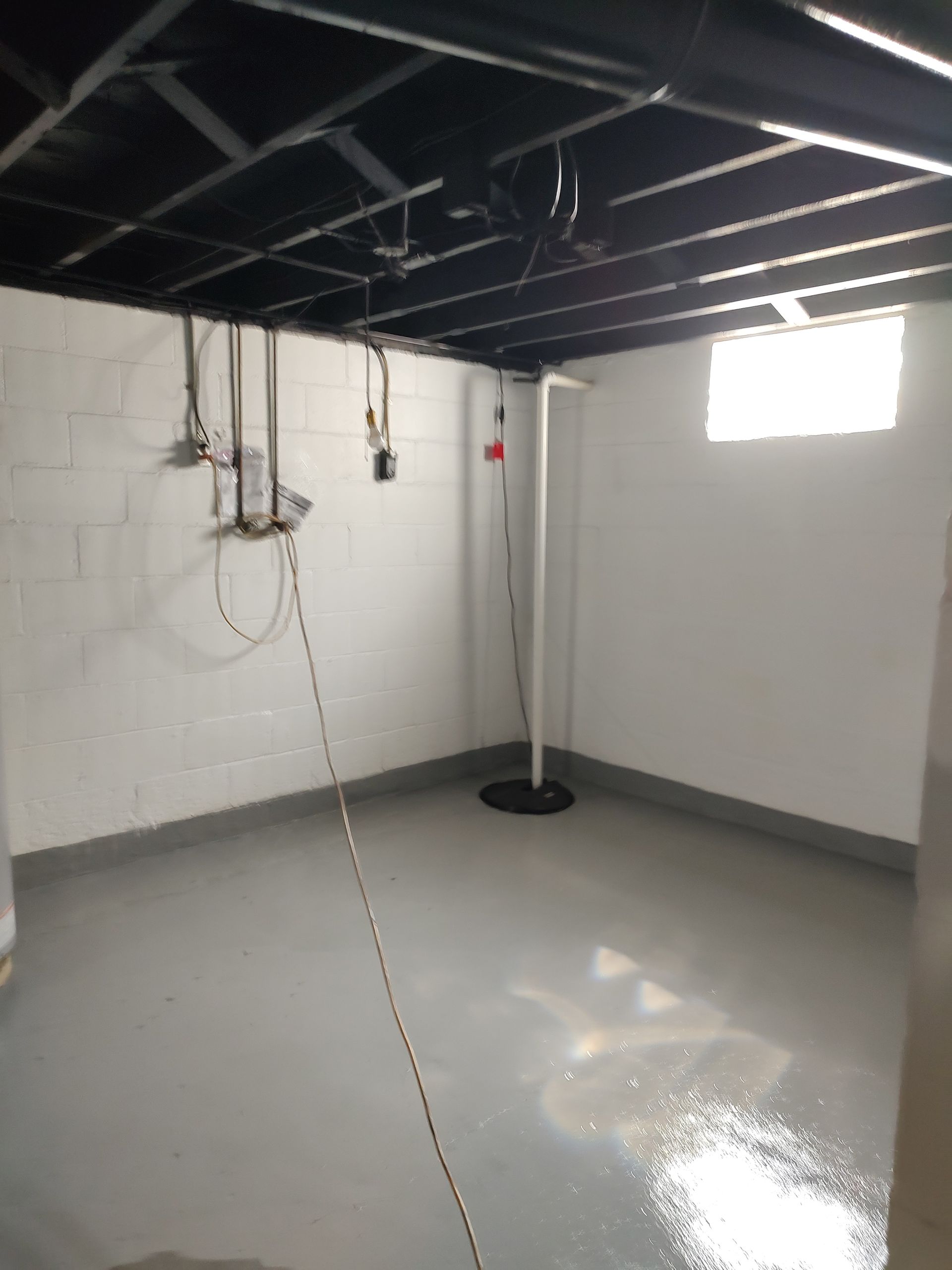 An empty basement with a window and a black ceiling