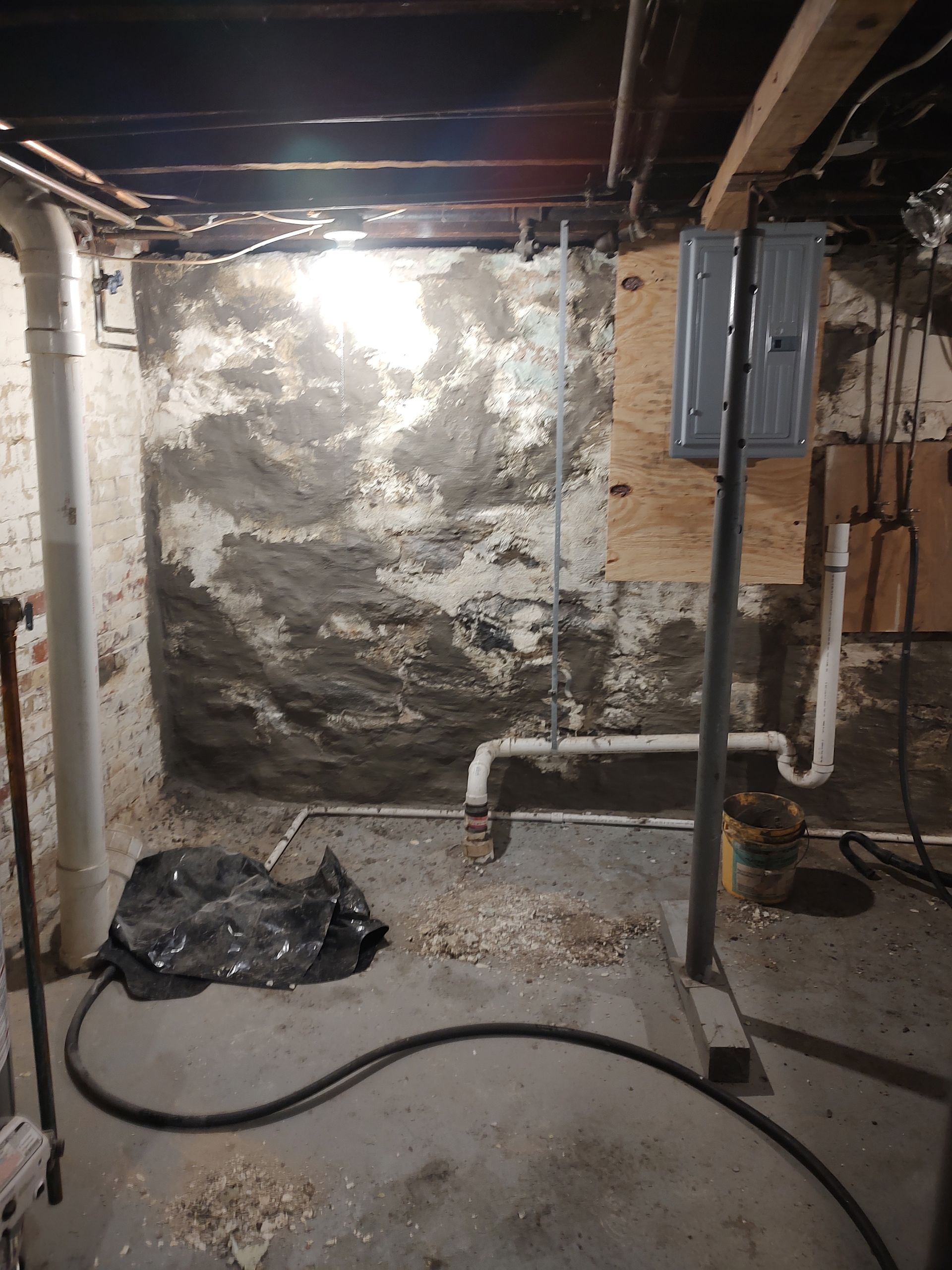 A basement with a lot of pipes and a light on the wall.