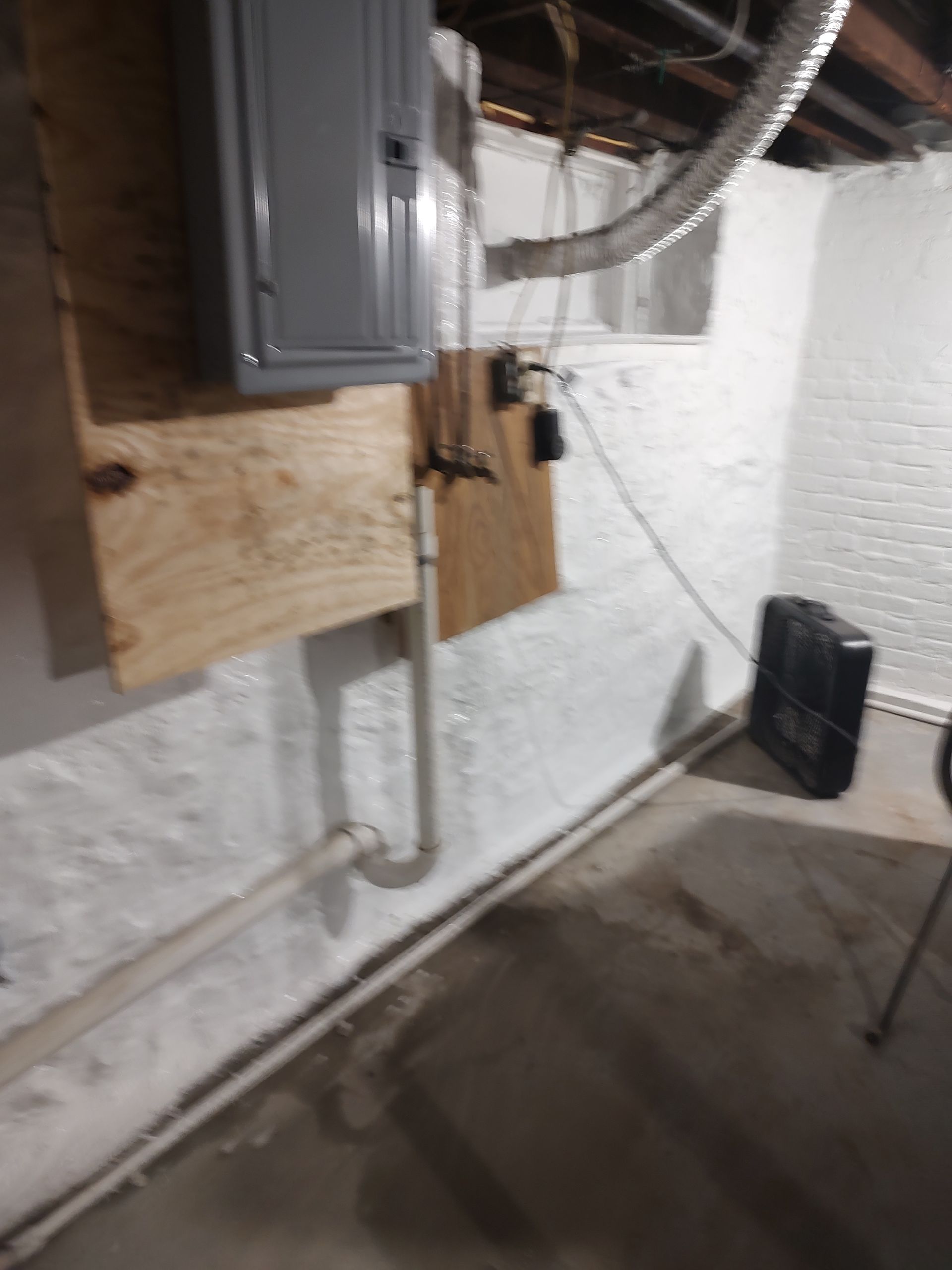 A basement with a gray box on the wall and a black box on the floor.