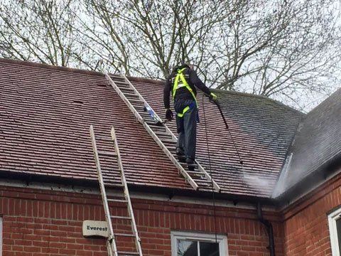 A man on a roof, jet washing the roof tiles
