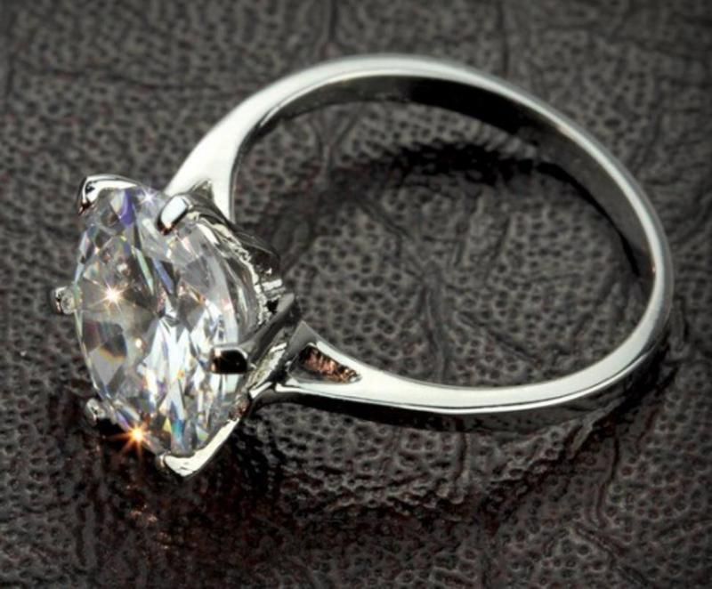 Diamond ring with a marquise-cut stone on a silver band, resting on a textured dark surface.
