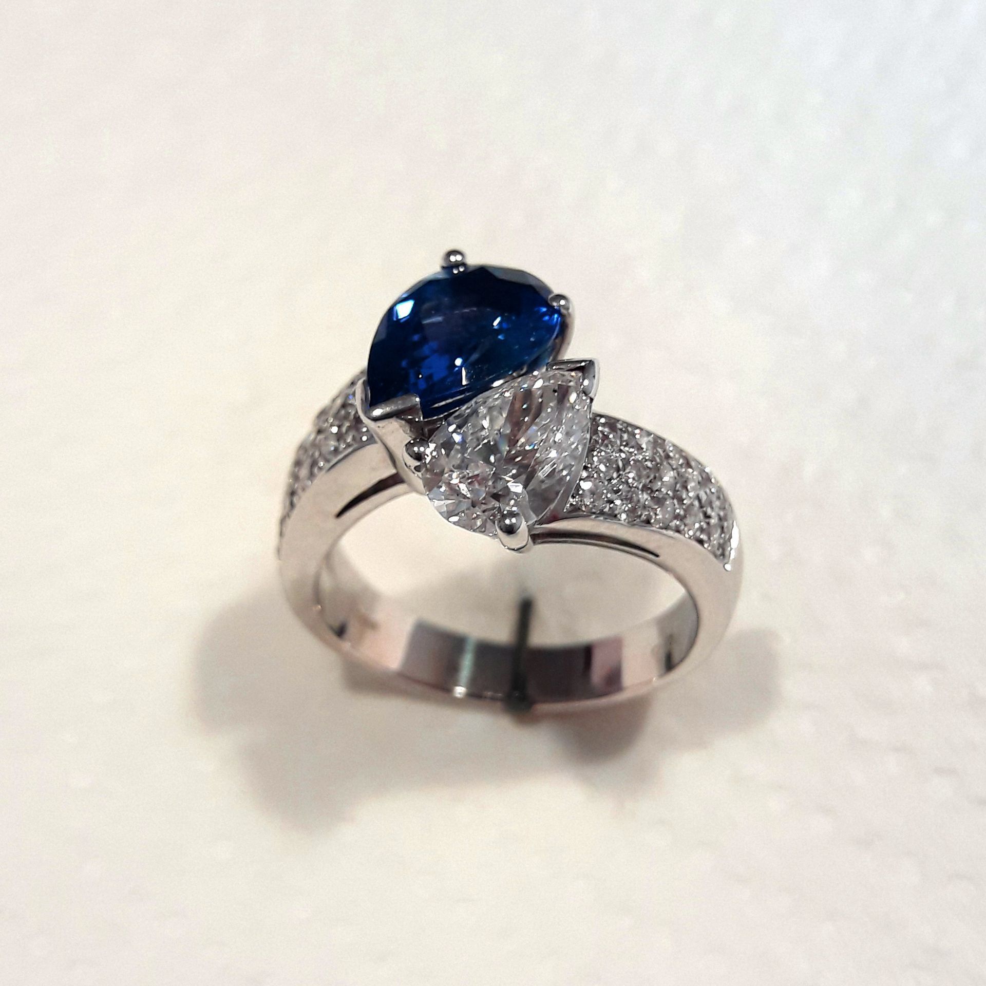 Ring with a pear-shaped blue gemstone and a pear-shaped clear gemstone, set in a band of small, clear stones.