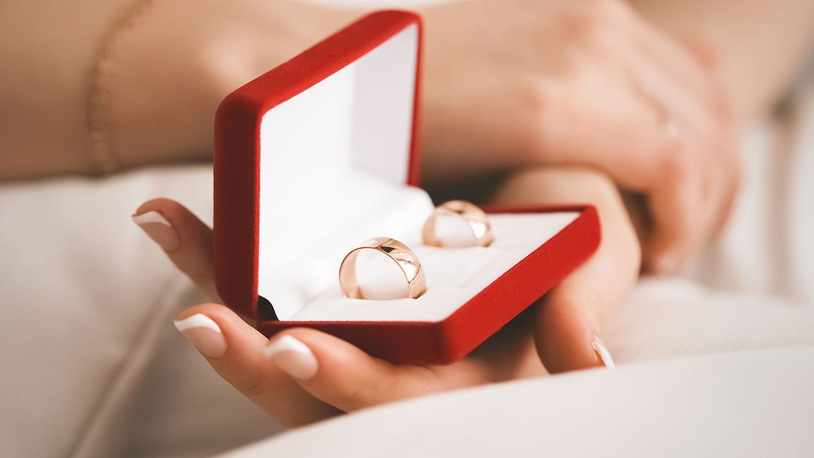 Woman's hands holding a red ring box with two gold wedding rings.