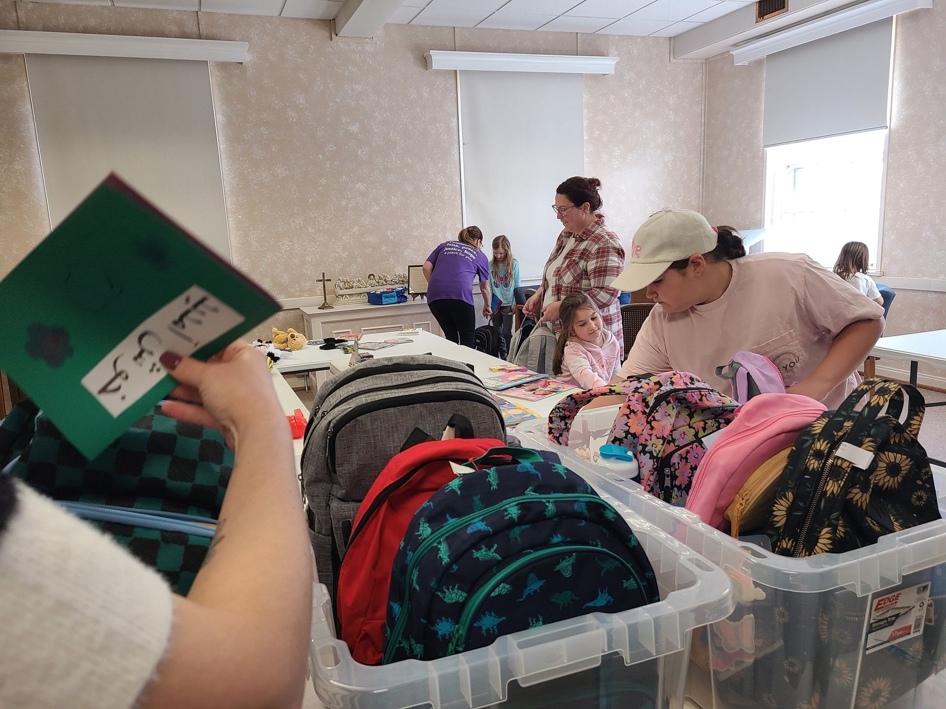 People packing backpacks in a room; includes kids and adults, backpacks, and folders.