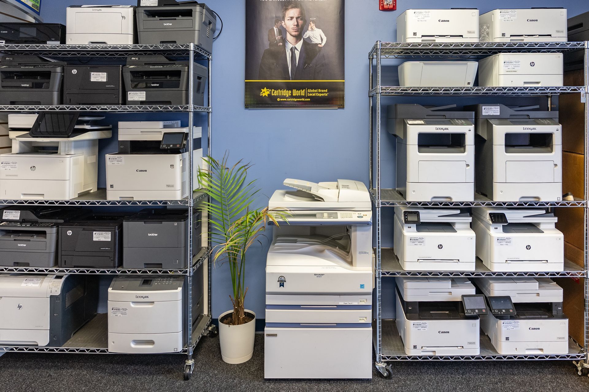 Person in a black mask fixing a printer, holding paper. Printer is white with color ink cartridges.