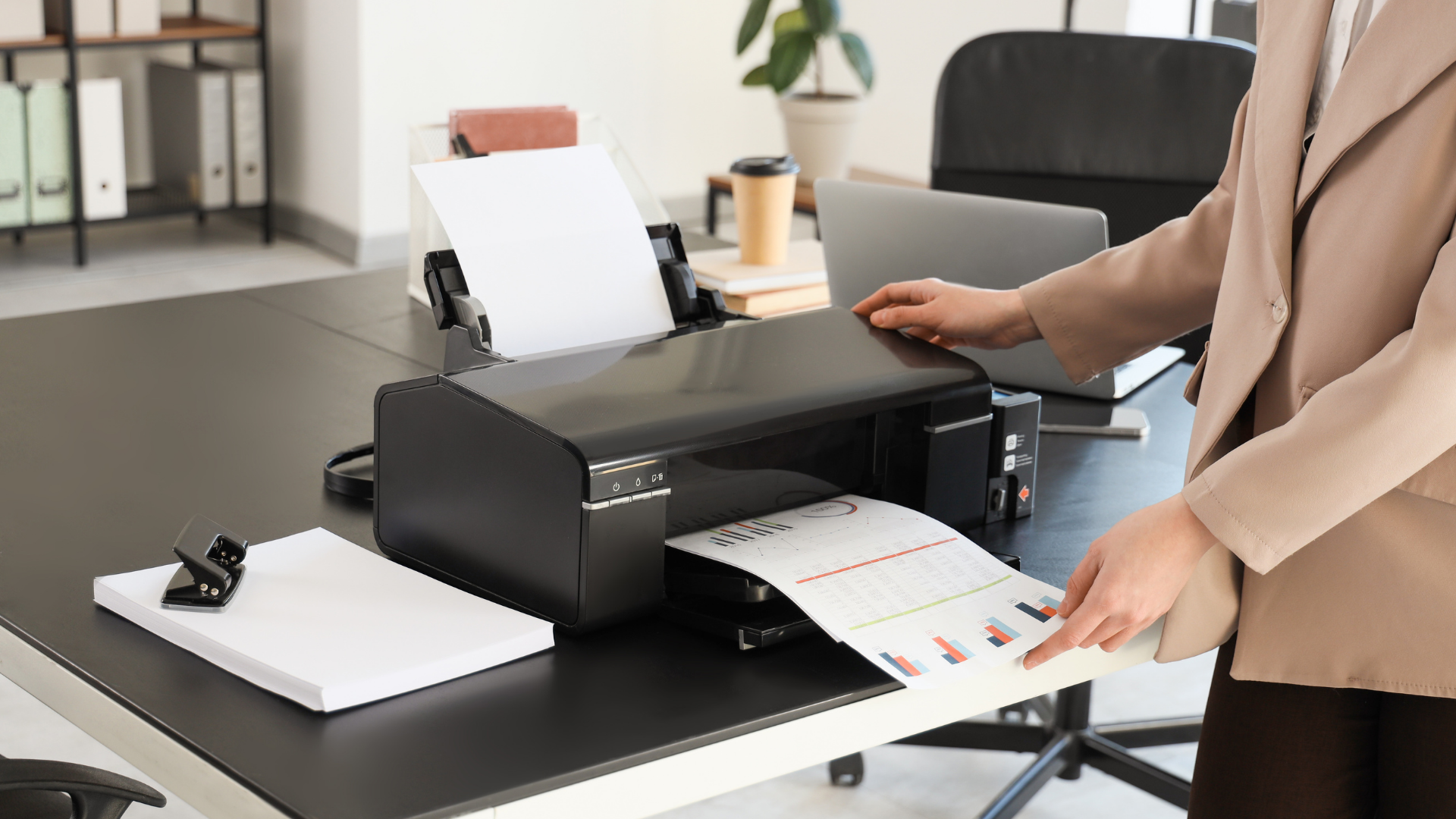 Person printing document from a black printer on a black desk in an office.
