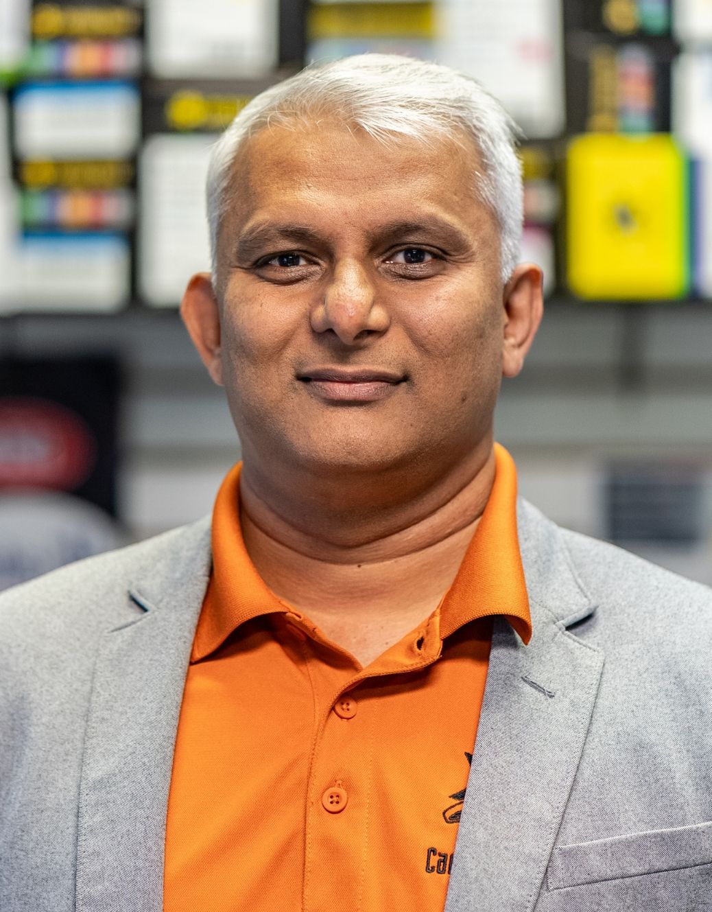 Woman wearing glasses in a blue polo shirt smiles, with hair pulled up.