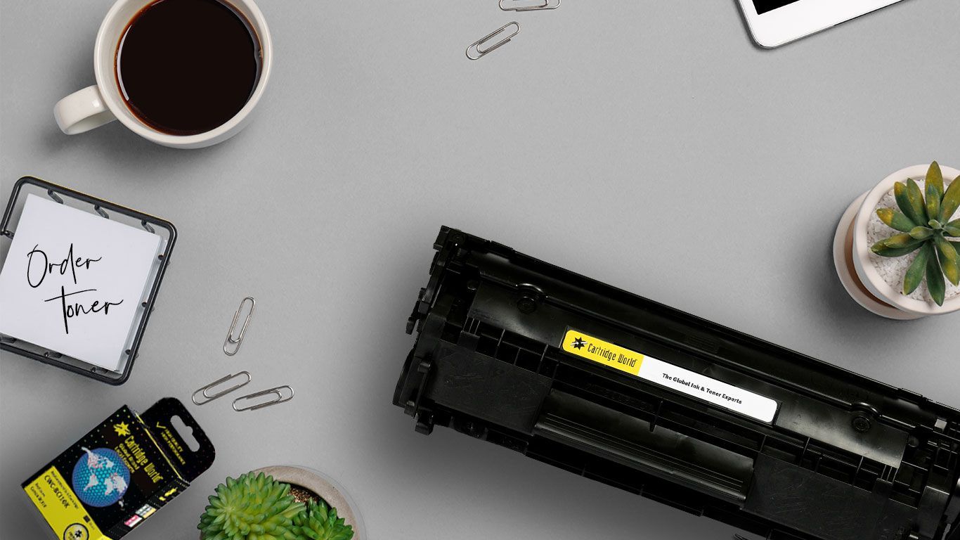 A toner cartridge is sitting on a table next to a cup of coffee.