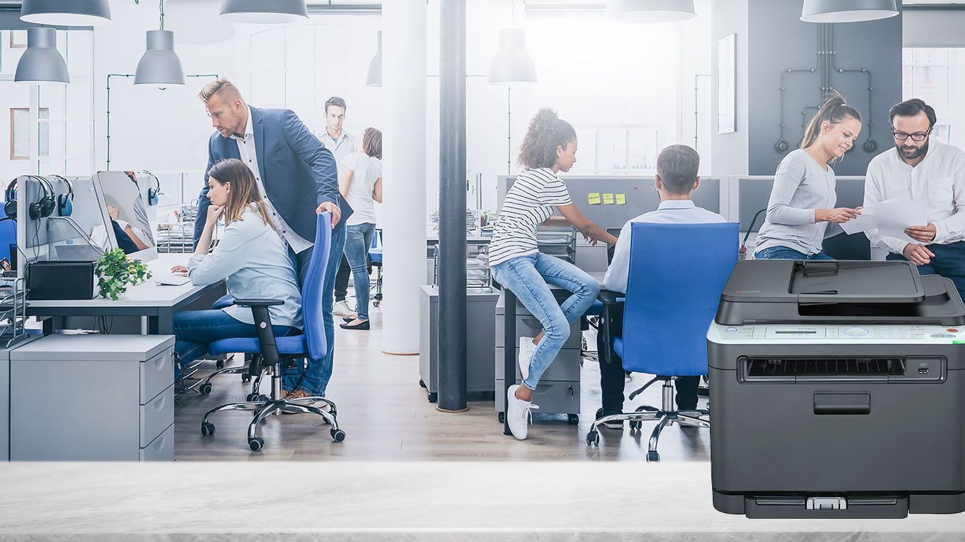 A group of people are sitting at desks in an office next to a printer.