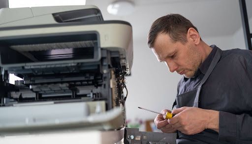 A man is fixing a printer with a screwdriver.