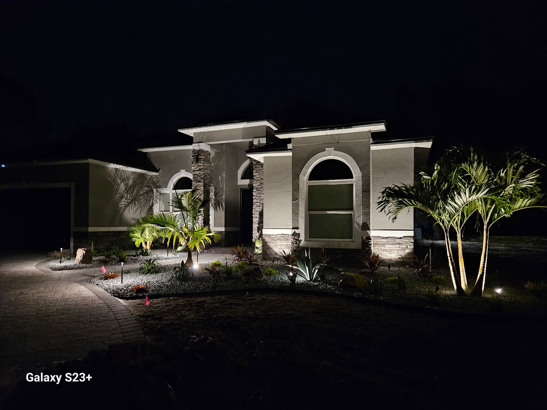 Night shot of a modern house entrance, illuminated with spotlights on the facade and landscaping; dark sky.