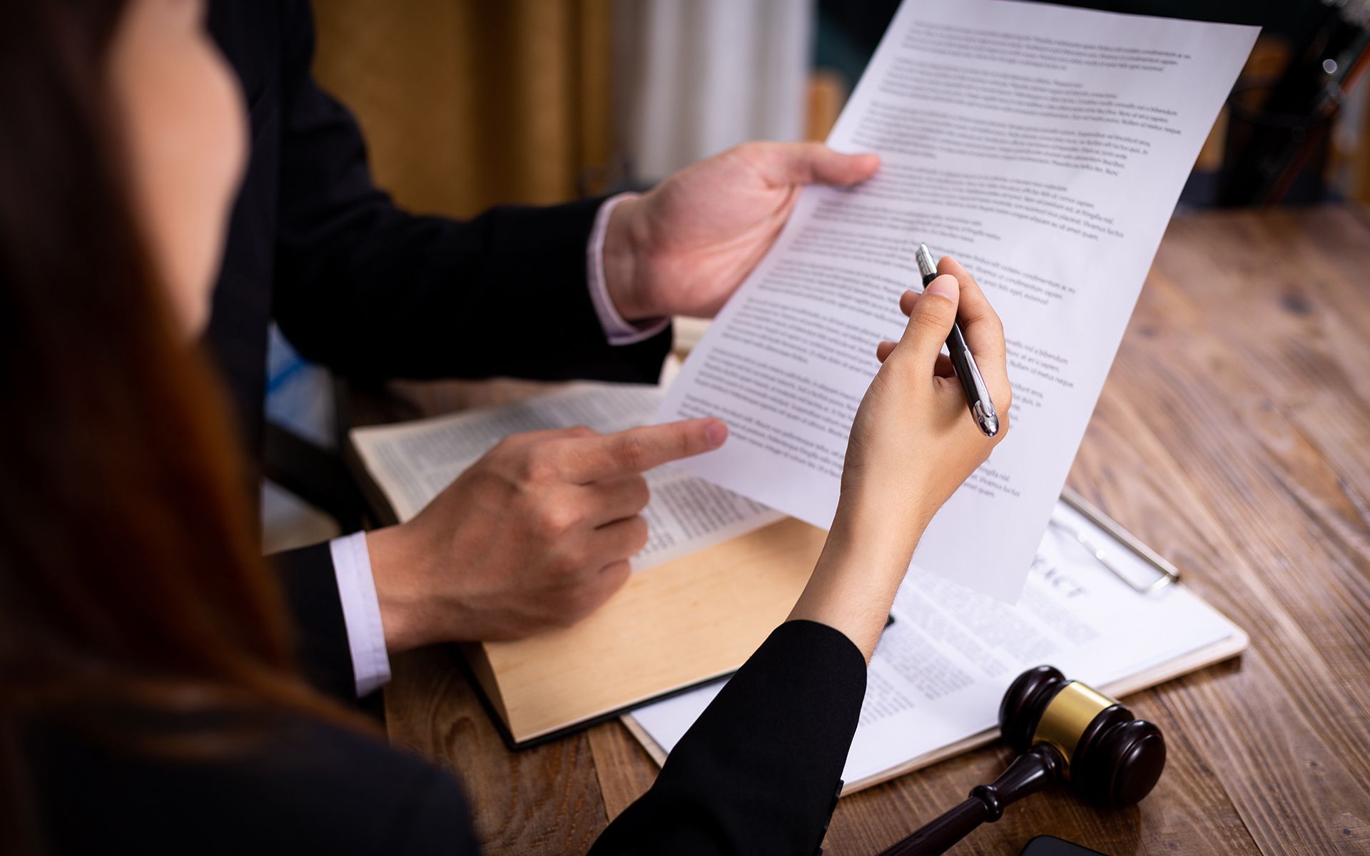 Lawyer pointing to document as person prepares to sign at desk with gavel.